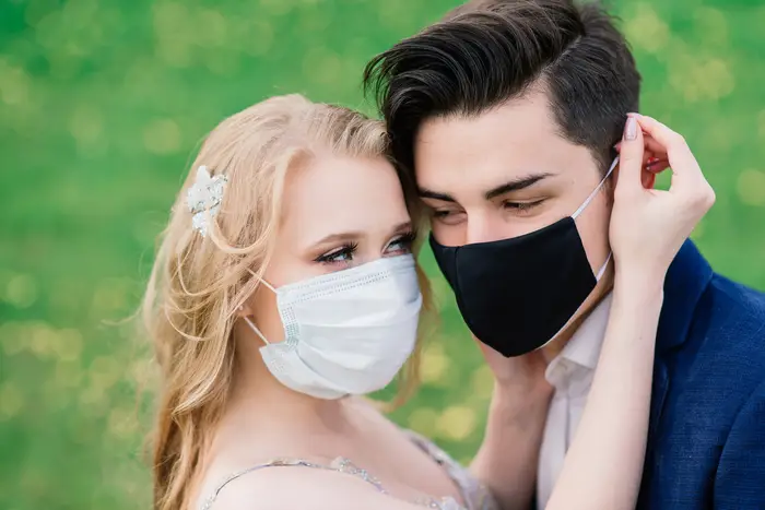 A stock photo showing a young loving couple walking in medical masks in the park during quarantine on their wedding day.